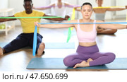 Asian woman sitting performs exercises with wide elastic band during Pilates multinational workout. Стоковое видео, видеограф Яков Филимонов / Фотобанк Лори