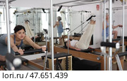 Young asian woman doing stretching exercises on Pilates reformer as part of injury rehabilitation course in modern fitness center. Стоковое видео, видеограф Яков Филимонов / Фотобанк Лори