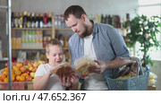 Friendly young dad and tween son wandering through supermarket with shopping basket in hand, examining packaged chicken and deciding on best option for family meal. Стоковое видео, видеограф Яков Филимонов / Фотобанк Лори