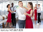 Confident man dancing waltz with female partner in red during group class. Стоковое фото, фотограф Яков Филимонов / Фотобанк Лори