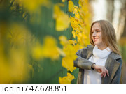Attractive woman with light brown hair near a green fence. Pretty woman in a gray coat. Beautiful young woman walks along the alley of the autumn park. Fall season. Yellow foliage. Autumn mood. Стоковое фото, фотограф Андрей Степанов / Фотобанк Лори