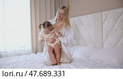 Attractive young woman and little cute girl are spending time together in bedroom at home. Mother with baby daughter lying on bed, hugging and having fun. Happy family concept. Mother's day footage. Стоковое видео, видеограф Ирина Михайличенко / Фотобанк Лори