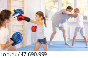 Tween girl in boxing gloves practicing punches on focus mitts in hands of mother. Стоковое фото, фотограф Яков Филимонов / Фотобанк Лори
