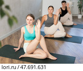 Woman and man performing Ardha Matsyendrasana position during group yoga training in fitness gym. Стоковое фото, фотограф Яков Филимонов / Фотобанк Лори