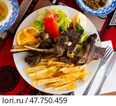 Delicious browned grilled lamb ribs served with crispy french fries and lettuce with tomato on plate, decorated with lemon. Стоковое фото, фотограф Яков Филимонов / Фотобанк Лори