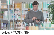Adult man with phone choosing medicines and hygiene products. Стоковое видео, видеограф Яков Филимонов / Фотобанк Лори