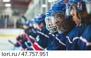 Players sit in a line on the bench, discussing tactics while preparing for their next turn on the ice. Стоковое AI-изображение, AI-художник Данила Большаков / Фотобанк Лори