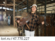 Female rancher carrying horse tack and saddle in horse farm. Стоковое фото, фотограф Яков Филимонов / Фотобанк Лори