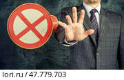 A man dressed in a formal suit holding a red and white no entry sign, signaling restriction or prohibition. Стоковое AI-изображение, AI-художник Данила Большаков / Фотобанк Лори