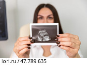 Happy young pregnant woman holding and showing ultrasound scan photo. Smiling mother with sonogram of her unborn baby. Concept of pregnancy. Maternity prenatal care. Стоковое фото, фотограф Ирина Михайличенко / Фотобанк Лори