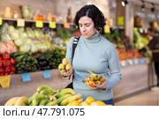 Female shopper carefully selects fresh bananas and other fruits in grocery supermarket. Стоковое фото, фотограф Яков Филимонов / Фотобанк Лори