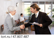 Smiling businessman with papers shaking hands with elderly woman. Стоковое фото, фотограф Яков Филимонов / Фотобанк Лори
