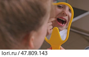 Lovely little girl looking in the mirror at her teeth after teeth surgery in a pediatric stomatology. A little girl sits in a dental chair and examines her cured teeth while looking in the mirror. Стоковое видео, видеограф Ирина Михайличенко / Фотобанк Лори