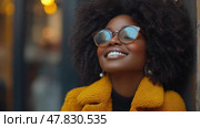 This young woman smiles contentedly, showcasing her fashion sense with a vibrant coat and glasses, enjoying a serene moment in an urban environment. Стоковое AI-изображение, AI-художник Данила Большаков / Фотобанк Лори