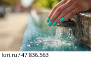 Hand gently touching flowing water from a fountain in a sunny park setting. Рука с яркими бирюзовыми ногтями слегка касается прохладной воды, текущей из фонтана. На заднем плане - пышный зеленый парк с солнечным светом, проникающим сквозь деревья и располагающим к отдыху. Стоковое AI-изображение, AI-художник Katsiaryna Repich / Фотобанк Лори