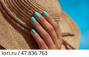 Enjoying summer vibes with a stylish straw hat and fresh nail color. Рука бережно держит соломенную шляпу под ярким солнцем, демонстрируя бирюзовый лак на ногтях. Безмятежный голубой фон отражает расслабляющую летнюю атмосферу. Стоковое AI-изображение, AI-художник Katsiaryna Repich / Фотобанк Лори