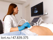 Happy pregnancy time, ultrasound concept. Pretty pregnant woman doing ultrasound scan in prenatal clinic. Professional female doctor screening of pregnant woman by ultrasound, looking at the screen. Стоковое фото, фотограф Ирина Михайличенко / Фотобанк Лори