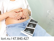Pregnant woman holding an ultrasound image of the baby. Close-up of pregnant belly and ultrasound photography in mother's hands. Untied and healthy pregnancy concept. Стоковое фото, фотограф Ирина Михайличенко / Фотобанк Лори