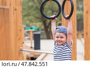 Lifestyle. A cute little boy is hanging on rings on a sports field in the fresh air. The concept of children's sports and physical development. Стоковое фото, фотограф Photojuli / Фотобанк Лори