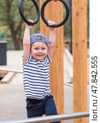 Lifestyle. A cute little boy is hanging on rings on a sports field in the fresh air. The concept of children's sports and physical development. Стоковое фото, фотограф Photojuli / Фотобанк Лори