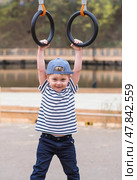 Lifestyle. A cute little boy is hanging on rings on a sports field in the fresh air. The concept of children's sports and physical development. Стоковое фото, фотограф Photojuli / Фотобанк Лори