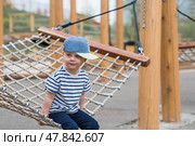 Lifestyle. A cute little boy is sitting in a hammock on a modern outdoor playground. The concept of family entertainment and leisure. Стоковое фото, фотограф Photojuli / Фотобанк Лори