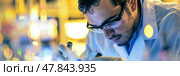 A scientist diligently notes observations while performing research in a vibrant laboratory illuminated by artificial lighting. Стоковое AI-изображение, AI-художник Данила Большаков / Фотобанк Лори