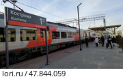 Lastochka train on platform of Kostroma railway station. People rushing to train. Modern carriages at low platform. Inscription on sign in Russian name of city.  Kostroma, Russia, April 17, 2025. Редакционное фото, фотограф Ирина / Фотобанк Лори