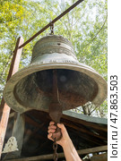 Large bronze bell is being rung by hand in a peaceful forest setting during the day. Стоковое фото, фотограф Климов Денис / Фотобанк Лори