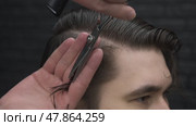 Barber carefully separates lock of hair from head of handsome brunette and carefully adjusts ends of hair to remove all excess. Close up. Стоковое видео, видеограф Strunov David / Фотобанк Лори