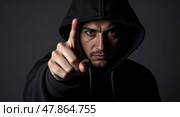 Dramatic lowkey portrait of a mysterious individual in dark hooded sweatshirt with extended finger pointing emphasizing confrontation and intensity. Стоковое AI-изображение, AI-художник Андрей Бакусов / Фотобанк Лори