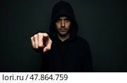 Mysterious hooded portrait with focused expression and confrontational gesture in lowkey lighting. Стоковое AI-изображение, AI-художник Андрей Бакусов / Фотобанк Лори
