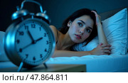 Contemplative woman lying in bed with vintage alarm clock capturing restlessness and insomnia in calming blue tones. Стоковое AI-изображение, AI-художник Андрей Бакусов / Фотобанк Лори