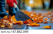 A person in red gloves sweeps colorful autumn leaves on a pathway, surrounded by trees displaying bright fall foliage. Стоковое AI-изображение, AI-художник Данила Большаков / Фотобанк Лори