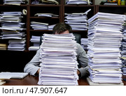 Офисный работник сидит за столом, его голова и лицо скрыты за огромными стопками бумаг. Стоковое AI-изображение, AI-художник Ольга Денис / Фотобанк Лори