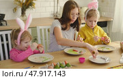 Children siblings painting Easter egg sitting together at table. Easter Family traditions. Teen girl teaching happy little brother and sister to dye, decorate eggs with paints. Preparation to holidays. Стоковое видео, видеограф Марина Демидюк / Фотобанк Лори