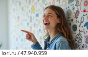A Young Woman Joyfully Laughs and Points to Her Left in Front of a Colorful Doodle Wall. Стоковое AI-изображение, AI-художник Sergey Grishin / Фотобанк Лори