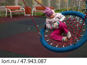 A cheerful five-year-old girl enjoys swinging on a colorful net swing at an autumn playground. Surrounded by bright foliage, she expresses curiosity and joy while engaging with her environment. Стоковое фото, фотограф Aleksandr Golubev / Фотобанк Лори