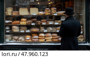 A man admires an array of breads and pastries in a bakery window during winter, surrounded by a snowy atmosphere in the city. Стоковое AI-изображение, AI-художник Данила Большаков / Фотобанк Лори