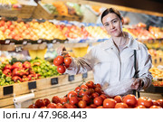 Woman carefully selects fresh tomatoes, standing near the counter in supermarket. Стоковое фото, фотограф Яков Филимонов / Фотобанк Лори