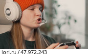 Focused teenage girl in orange beanie and headset plays video game, holding controller with concentration. Concept of female gamer, competitive eSports, online gaming, and modern digital lifestyle. Стоковое видео, видеограф Енваев Андрей / Фотобанк Лори