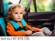 The child is sitting in the car, securely fastened with seat belts in the car seat. Стоковое AI-изображение, AI-художник Ирина Старикова / Фотобанк Лори