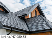 A well-constructed roof of a contemporary home highlights the unique tile pattern beneath a blue sky with scattered clouds. Стоковое AI-изображение, AI-художник Данила Большаков / Фотобанк Лори