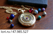 Vintage pocket watch resting on wooden table surrounded by colorful gemstones and a leather-bound book. Стоковое AI-изображение, AI-художник Сергей Толмачёв / Фотобанк Лори