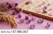 Unique amethyst stones with symbols beside dried flowers and a wooden board displaying markings on a pink background. Стоковое AI-изображение, AI-художник Сергей Толмачёв / Фотобанк Лори