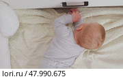 A toddler with red hair reaches for the black handle of a white box while lying on the floor. Top view. The curious expression on his face captures the essence of the child's exploration. Стоковое видео, видеограф Воловодов Владимир / Фотобанк Лори