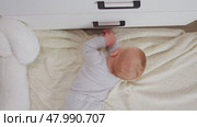 A cute baby with light red hair reaches for the handle of a crate while lying on a soft, fluffy blanket. His curious expression captures the essence of childlike exploration. Top view. Стоковое видео, видеограф Воловодов Владимир / Фотобанк Лори