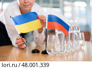 Unrecognizable girl sets midget flags of Russia and Ukraine before international negotiations. Стоковое фото, фотограф Яков Филимонов / Фотобанк Лори