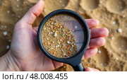 Hand holding a magnifying glass over a pile of sand. Microplastic. Стоковое AI-изображение, AI-художник Sergey Grishin / Фотобанк Лори