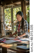 A woman focuses on writing while surrounded by sunlight and a rustic cabin atmosphere. Стоковое AI-изображение, AI-художник Данила Большаков / Фотобанк Лори